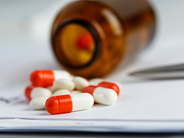 red and white tablets spilled out of brown medicine bottle